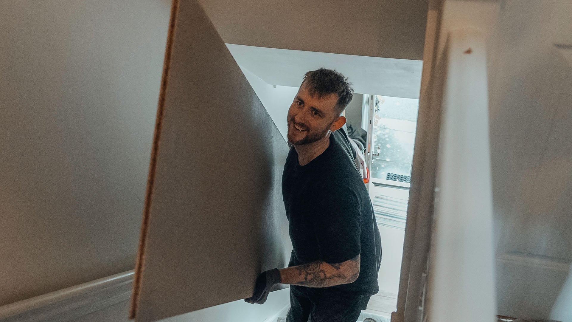 Loft installer carrying large floorboard up stairs — Loft-Trac