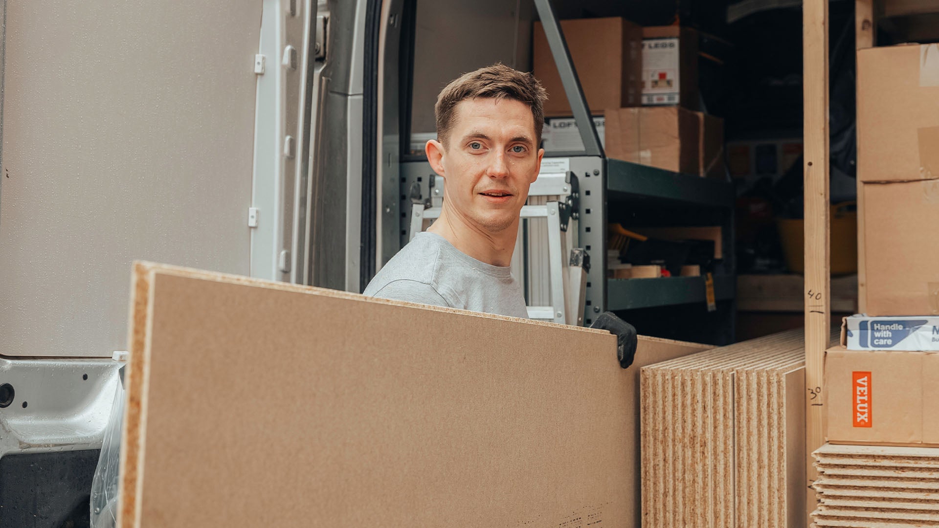 Loft installer smiling at camera carrying floorboard — Loft-Trac